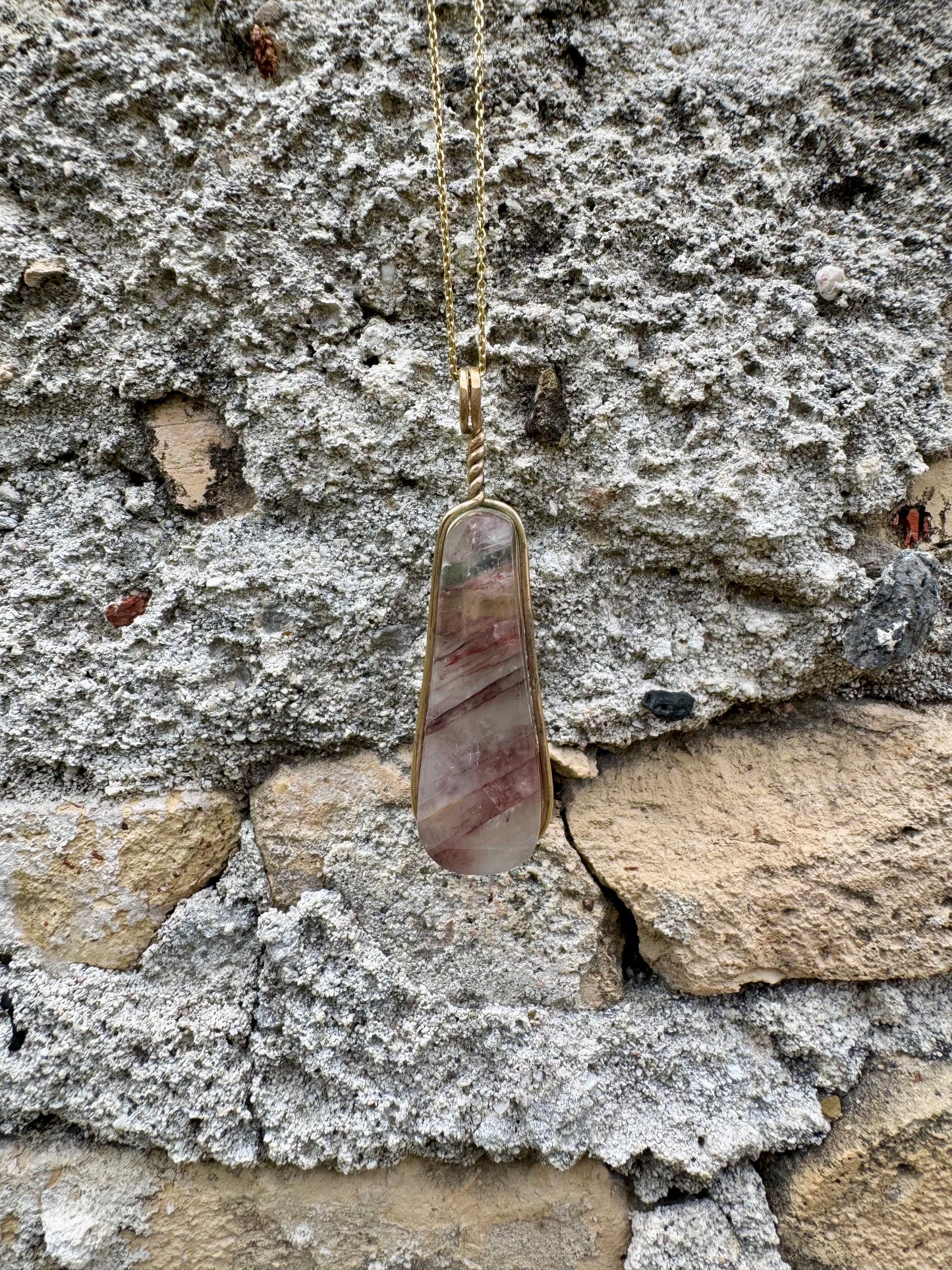 Necklace with an agate stone gold-wrapped pendant against a stone wall background