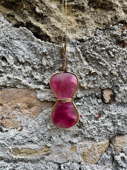 Pink stone pendant on a chain against a textured stone wall background