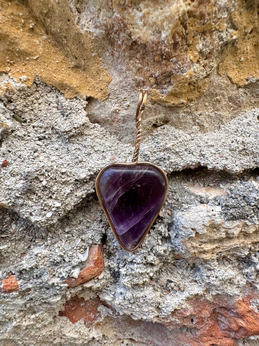 Amethyst triangular-shaped pendant on gold chain against a stone wall background