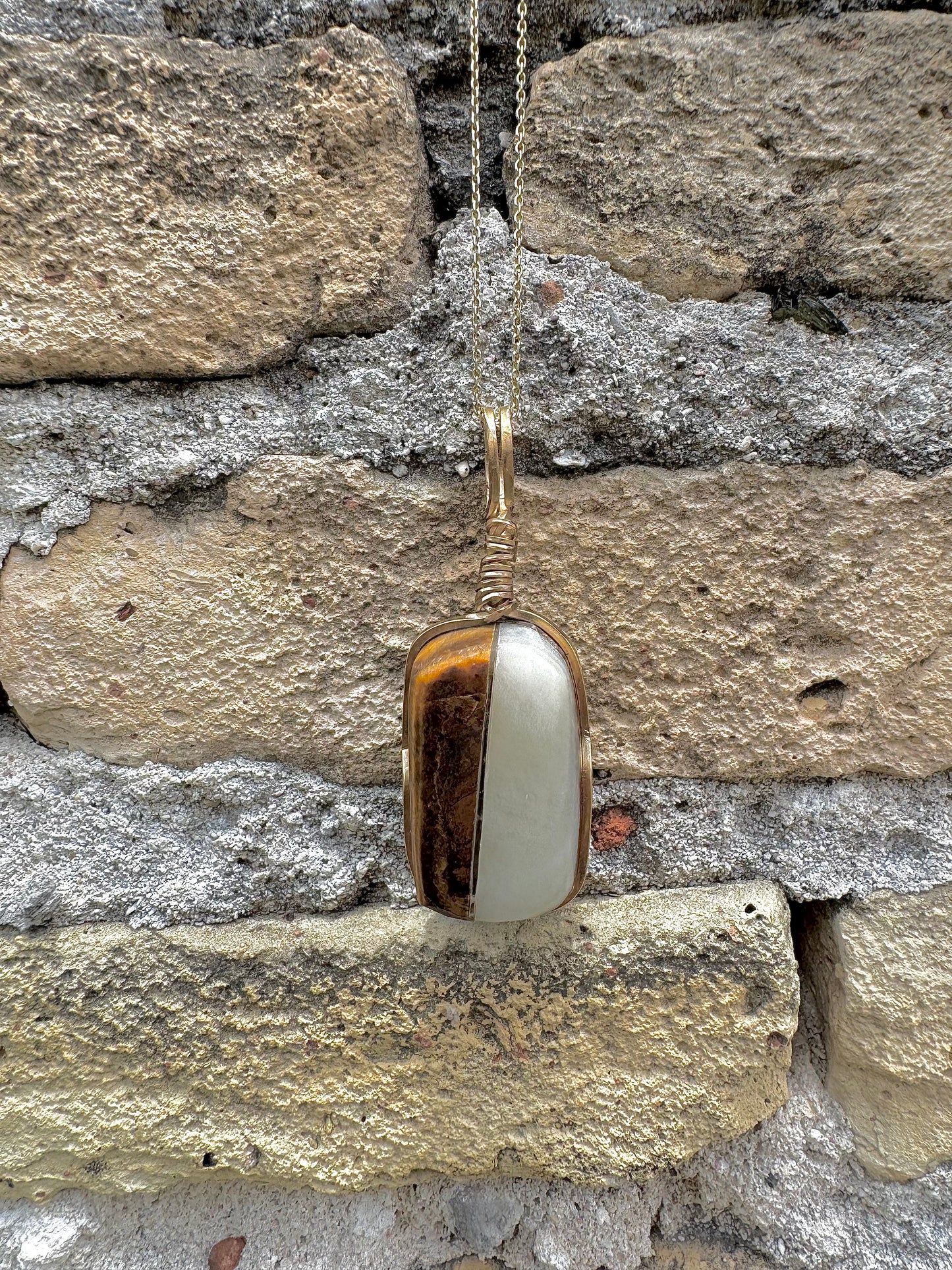 Gold pendant with a white stone against a stone wall background