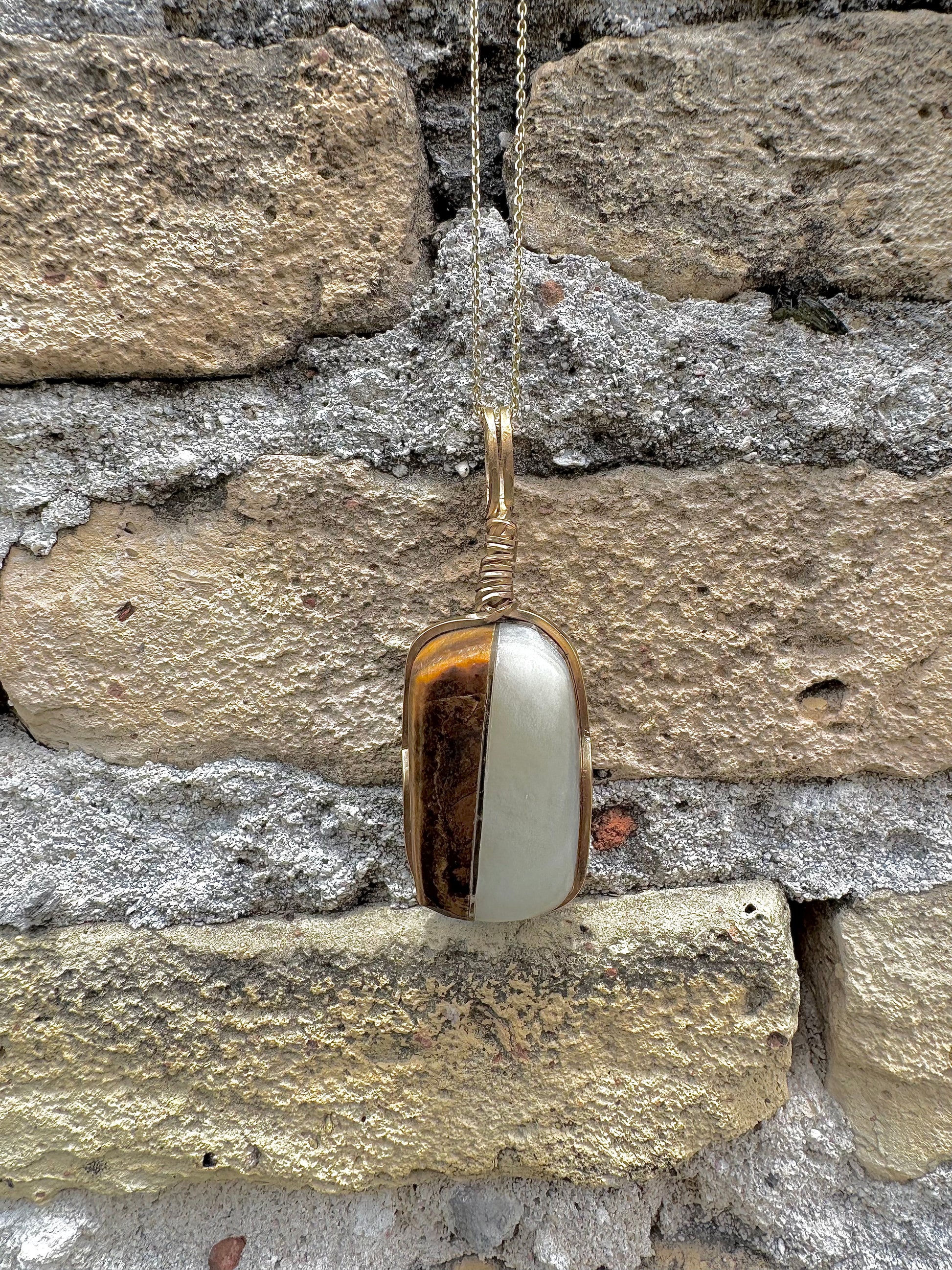 Gold pendant with a white stone against a stone wall background