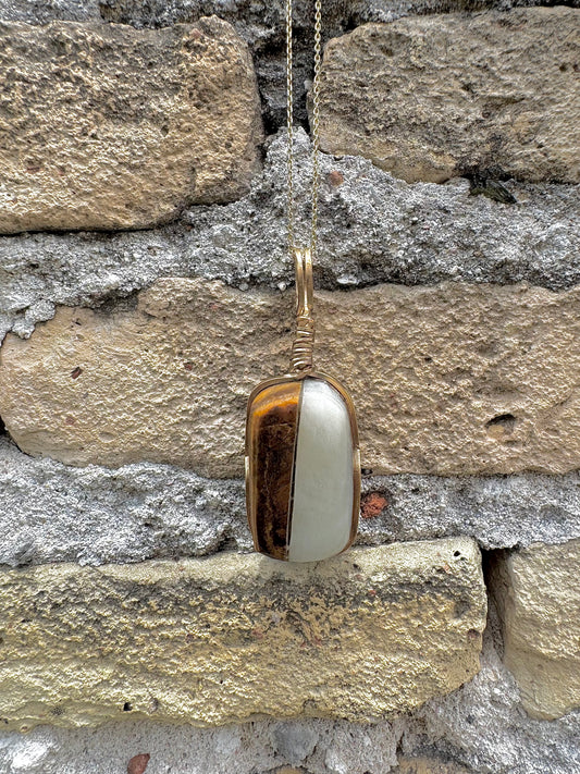 Gold pendant with a white stone against a stone wall background