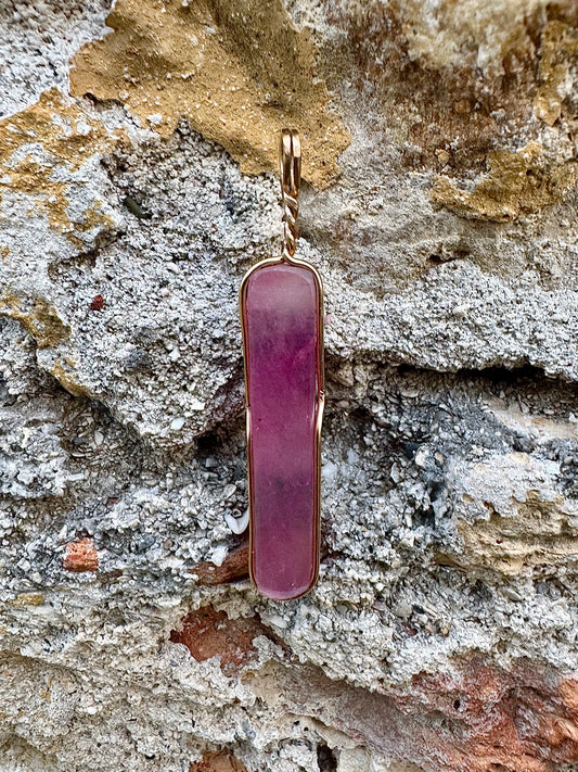 Pink pendant with gold frame on a textured stone background