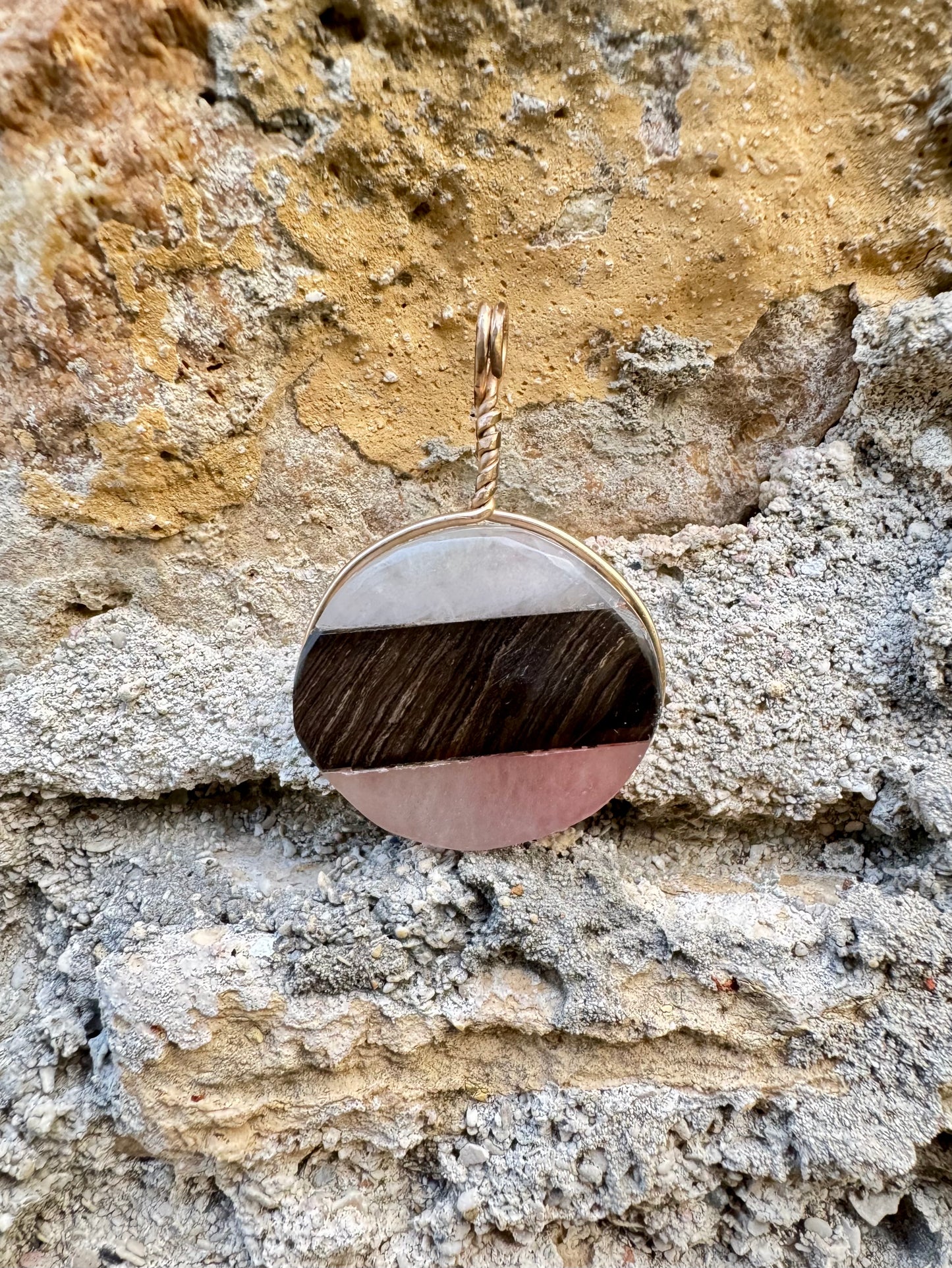 Round pendant with wooden and pink stone design on a textured stone surface