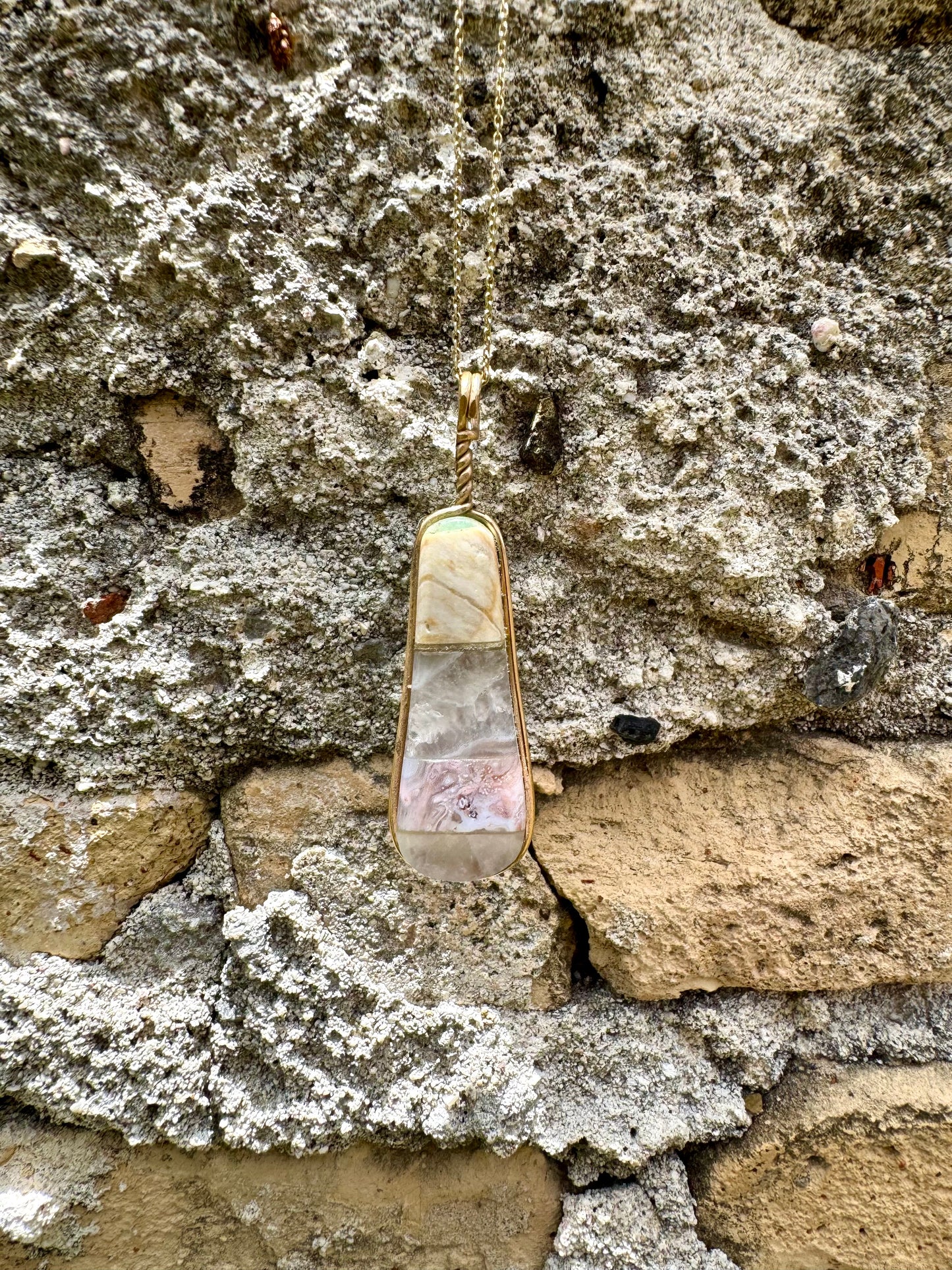 Gold necklace with a pendant on a stone wall
