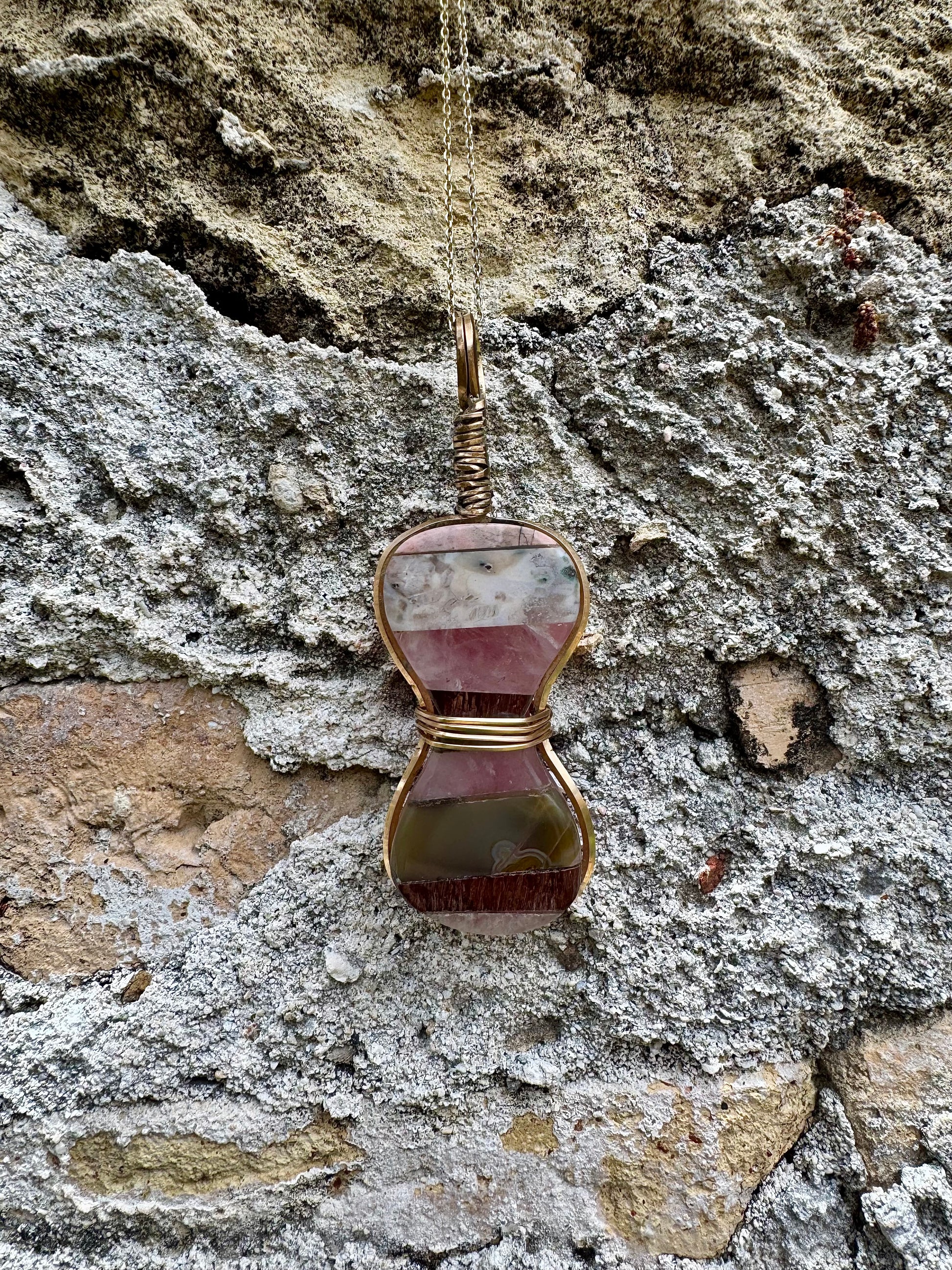 Gold-wrapped hourglass semi-precious gemstone pendant on stone background